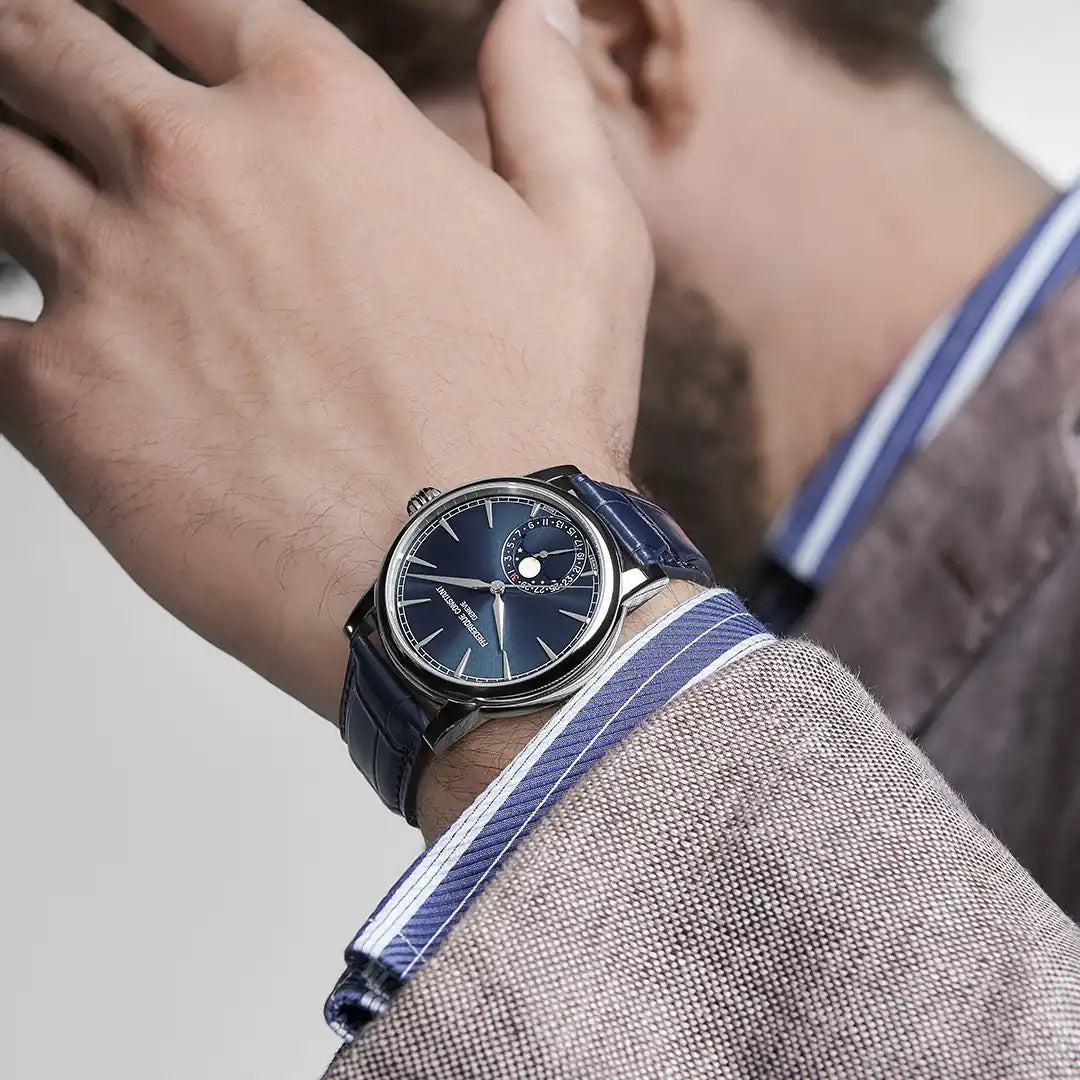 Mann trägt die Manufacture Classic Moonphase Date in der dunkelblauen Farbvariante von Frederique Constant am dunkelblauen Lederband an seinem Handgelenk