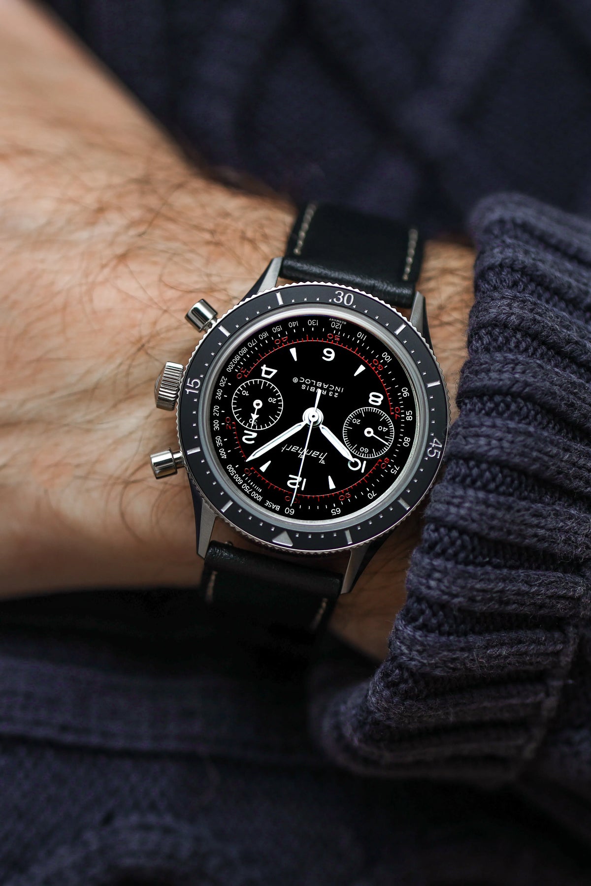 Mann trägt den Hanhart 415 ES Pure Chronographen in Edelstahl mit weißen und roten Details am Lederband und präsentiert die Uhr in die Kamera