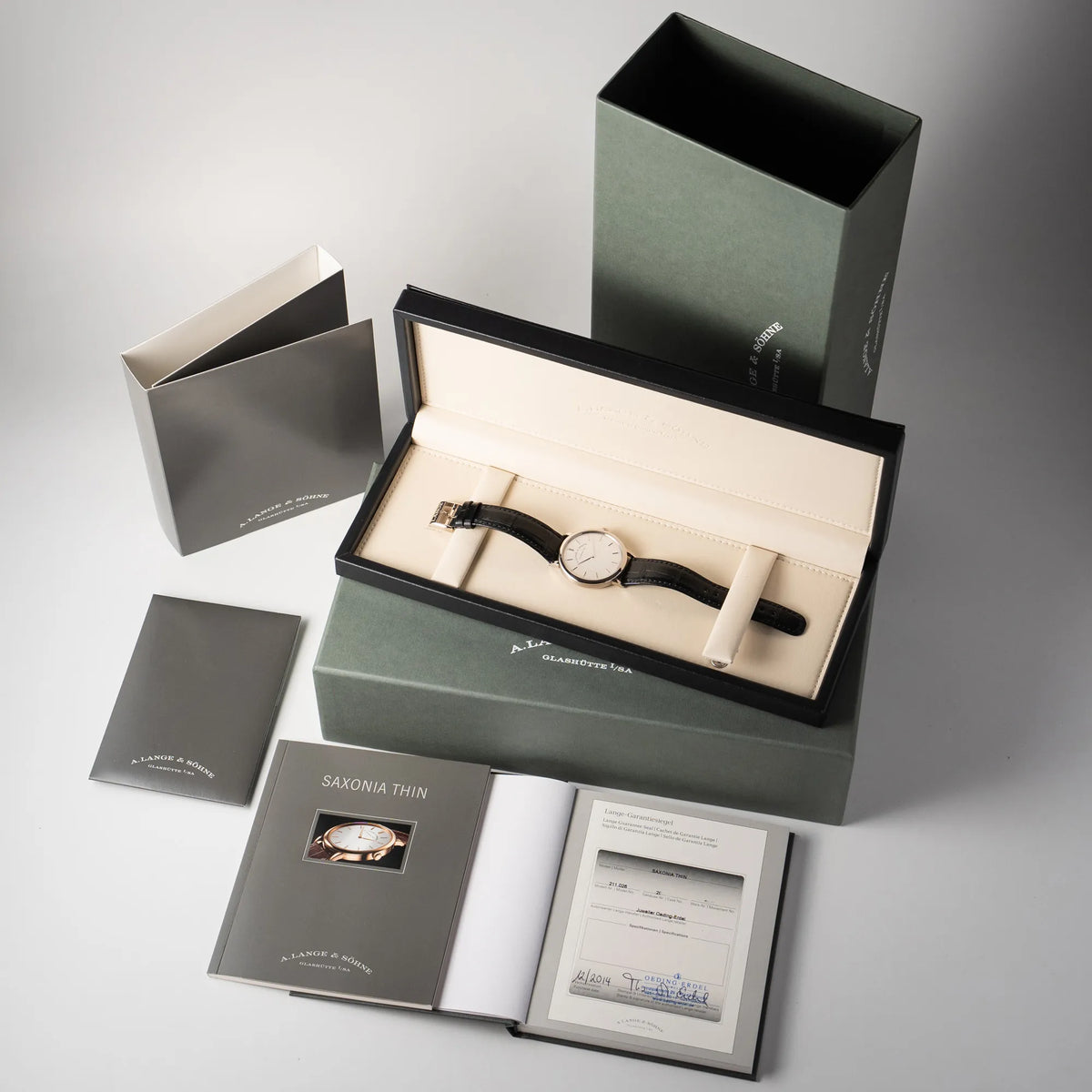Lieferumfang zu der A.Lange Söhne Saxonia Thin der Referenz 211.026 im Weißgold-Gehäuse mit weiß-silbernem Zifferblatt am schwarzen Lederarmband, bestehend aus Box mit Umkarton, Booklets, Anleitung und original Papieren