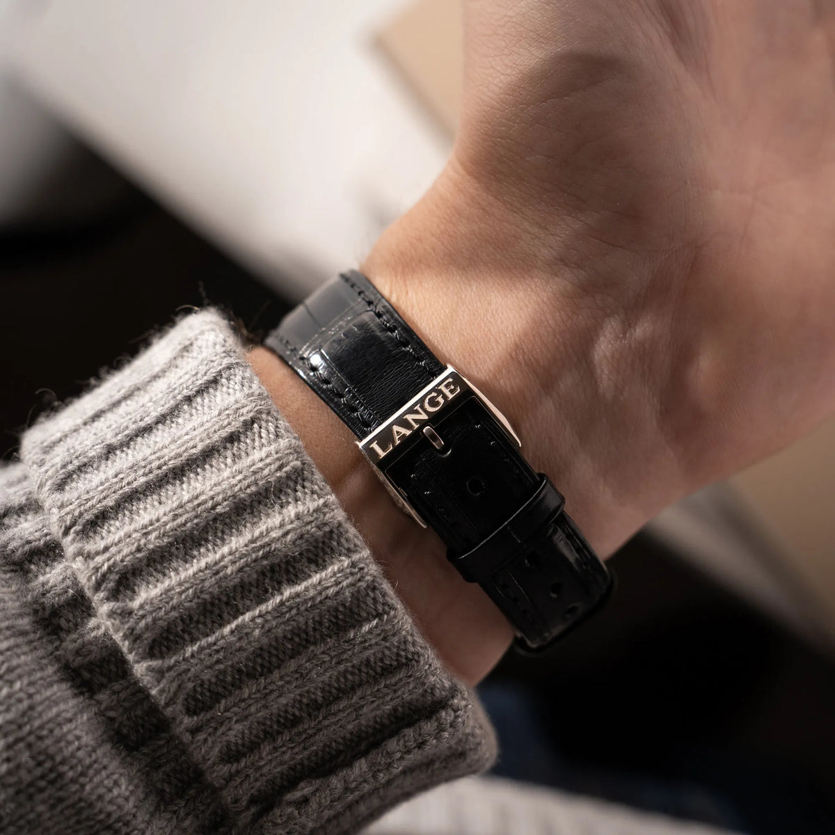 Mann präsentiert die Dornschliesse mit "Lange"-Schriftzug von der A.Lange Söhne Saxonia Thin der Referenz 211.026 im Weißgold-Gehäuse mit weiß-silbernem Zifferblatt am schwarzen Lederarmband