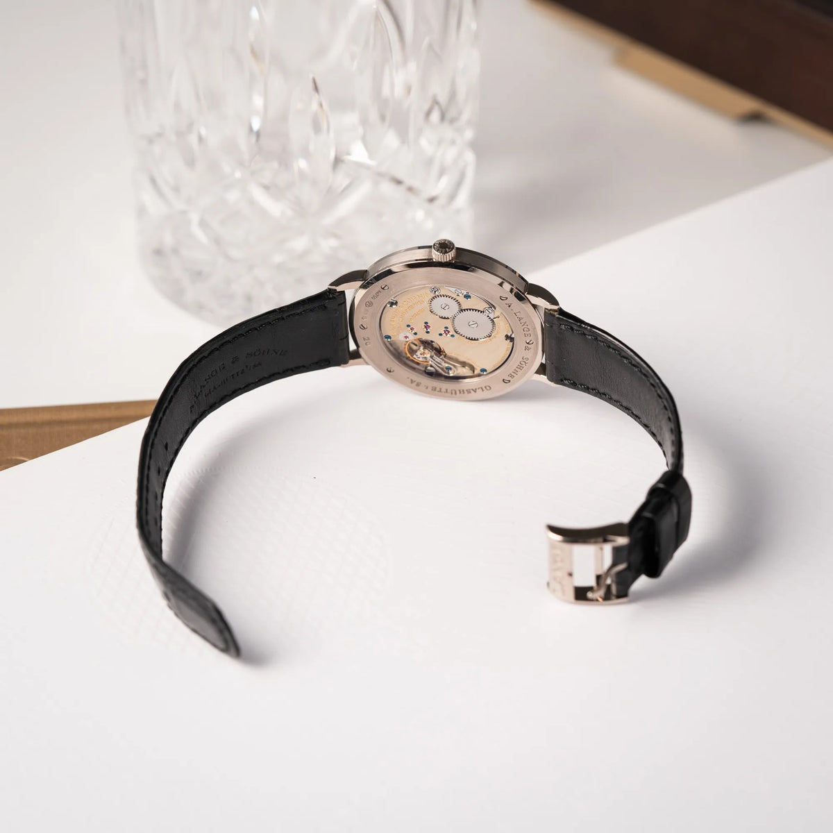 Produktfotografie zeugt den Gehäuseboden mit Sichtglas von der A.Lange Söhne Saxonia Thin der Referenz 211.026 im Weißgold-Gehäuse mit weiß-silbernem Zifferblatt am schwarzen Lederarmband