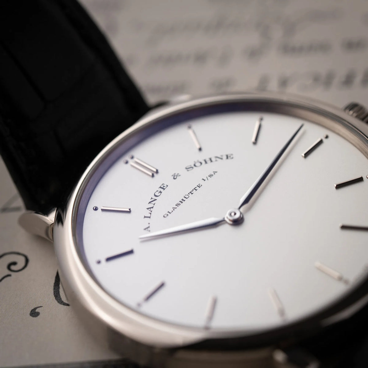 Detailaufnahme zeigt den Schriftzug ei 12 Uhr von der A.Lange Söhne Saxonia Thin der Referenz 211.026 im Weißgold-Gehäuse mit weiß-silbernem Zifferblatt am schwarzen Lederarmband