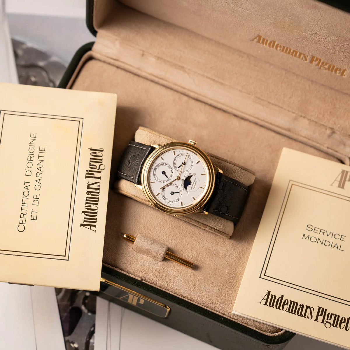 Audemars Piguet Quantième Perpétual der Referenz 5548BA mit 36mm-Gelbgold-Gehäuse und weißem Zifferblatt an einem schwarzen Lederband zusammen moit der Uhrenbox, dem gelbgoldenen Stellstift und den original Papieren