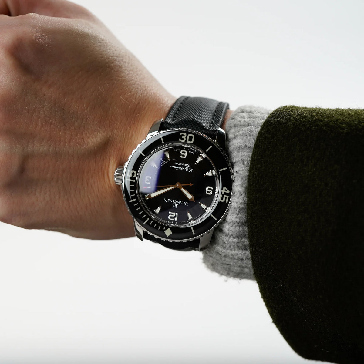 Mann trägt die. Blancpain Fifty Fathoms in Schwarz am Nylon-Band an seinem Handgelenk und präsentiert diese kopfüber der Kamera