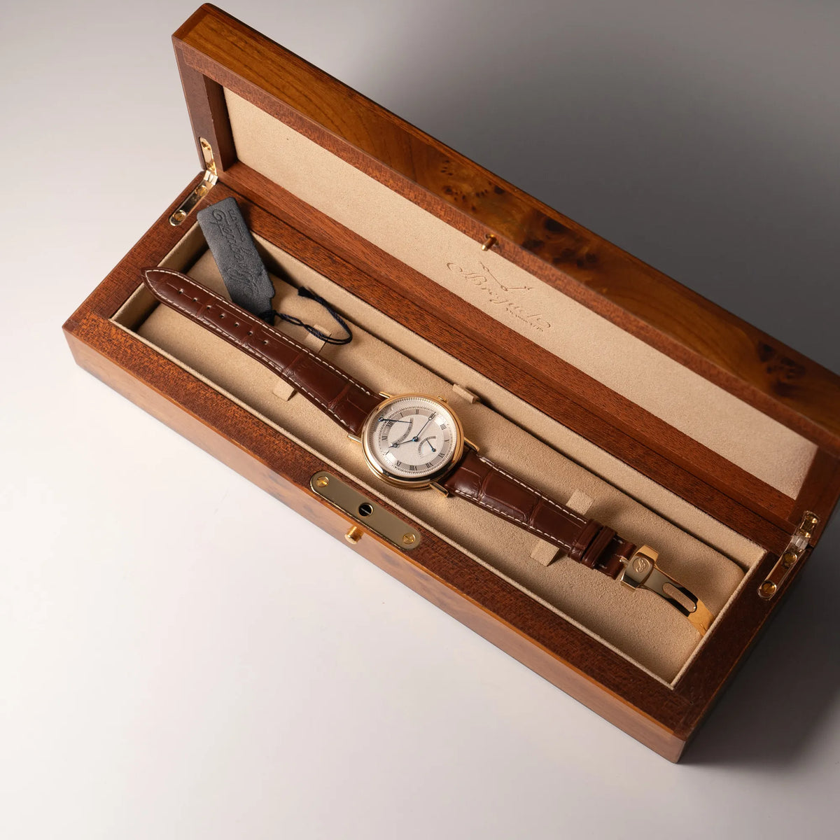 Gelbgoldene Breguet Armbanduhr des Models Classic Retrograde 5207 am braunen Lederband liegt in der originalen Uhrenbox aus Wurzelholz
