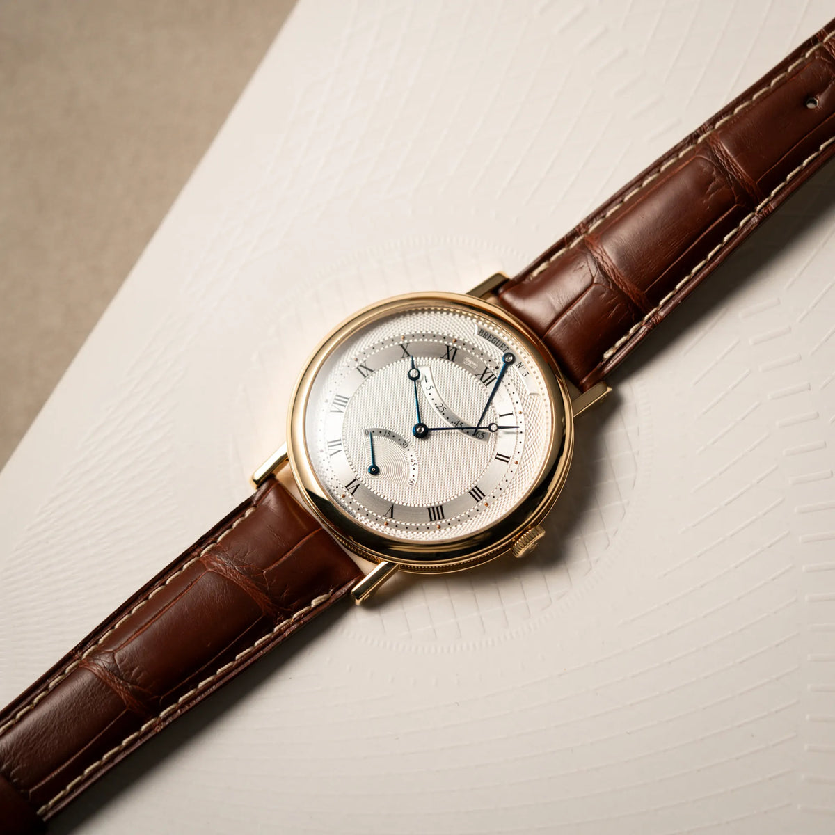 Produktfotografie der gelbgoldenen Breguet Armbanduhr des Models Classic Retrograde 5207 am braunen Lederband
