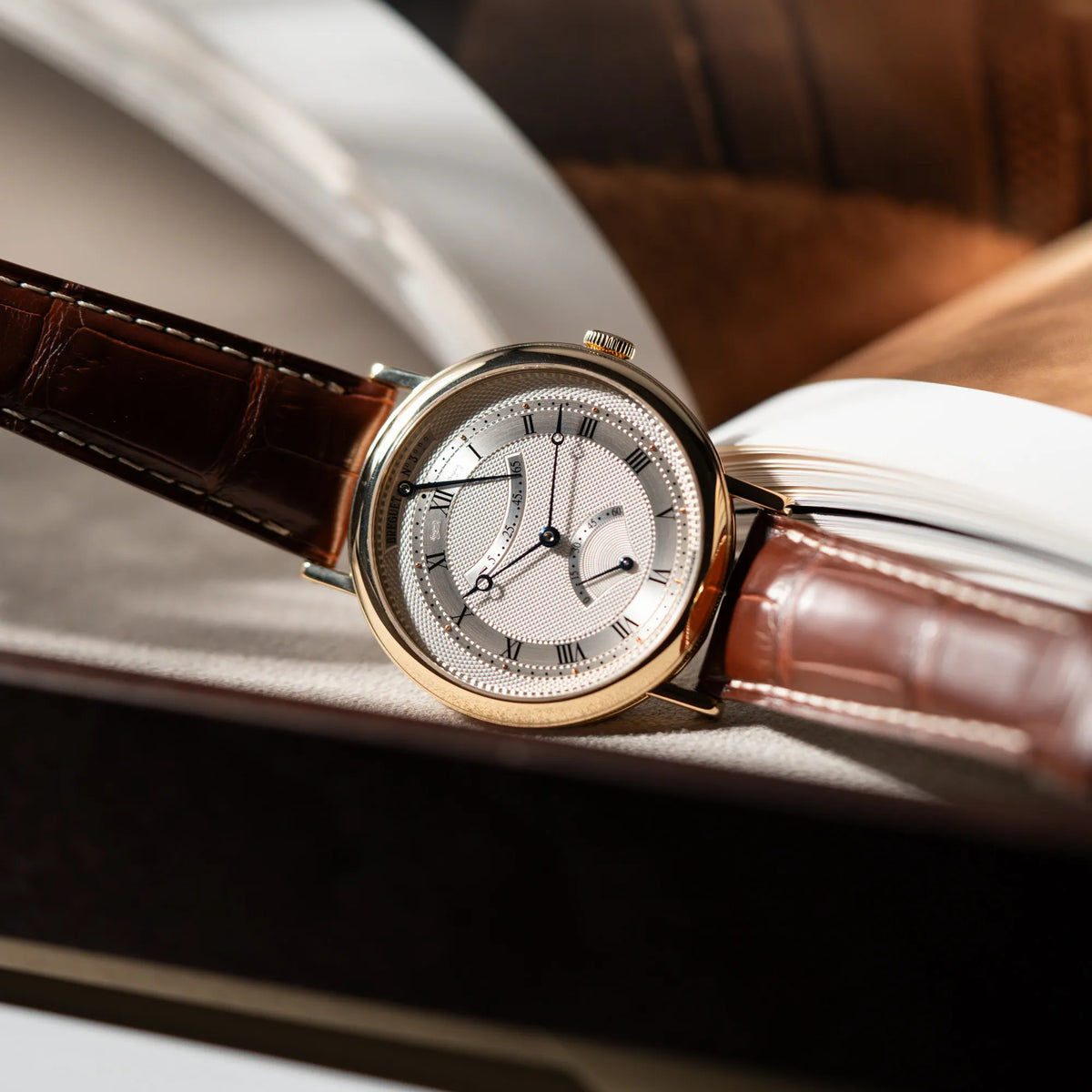 Produktfotografie der gelbgoldenen Breguet Armbanduhr des Models Classic Retrograde 5207 am braunen Lederband