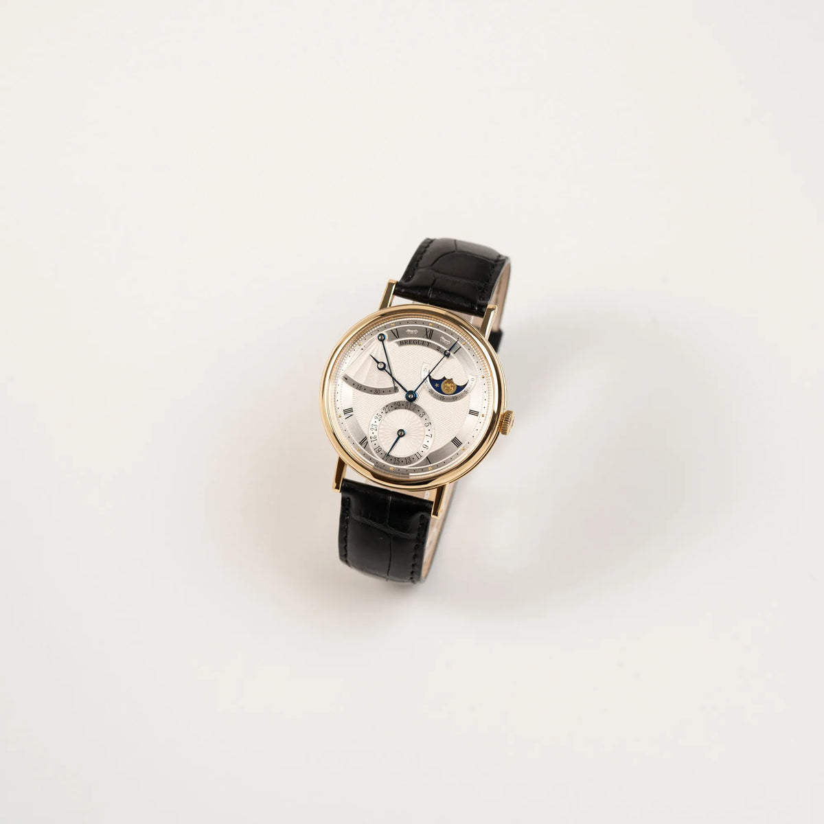 Leicht schräge Ansicht der Breguet Classique 7137BA mit einem Gelbgoldgehäuse in klassischer Form mit einem silbernen Zifferblatt mit jeweils einem anderen handgefertigten Guilloche-Muster für jede Komplikation