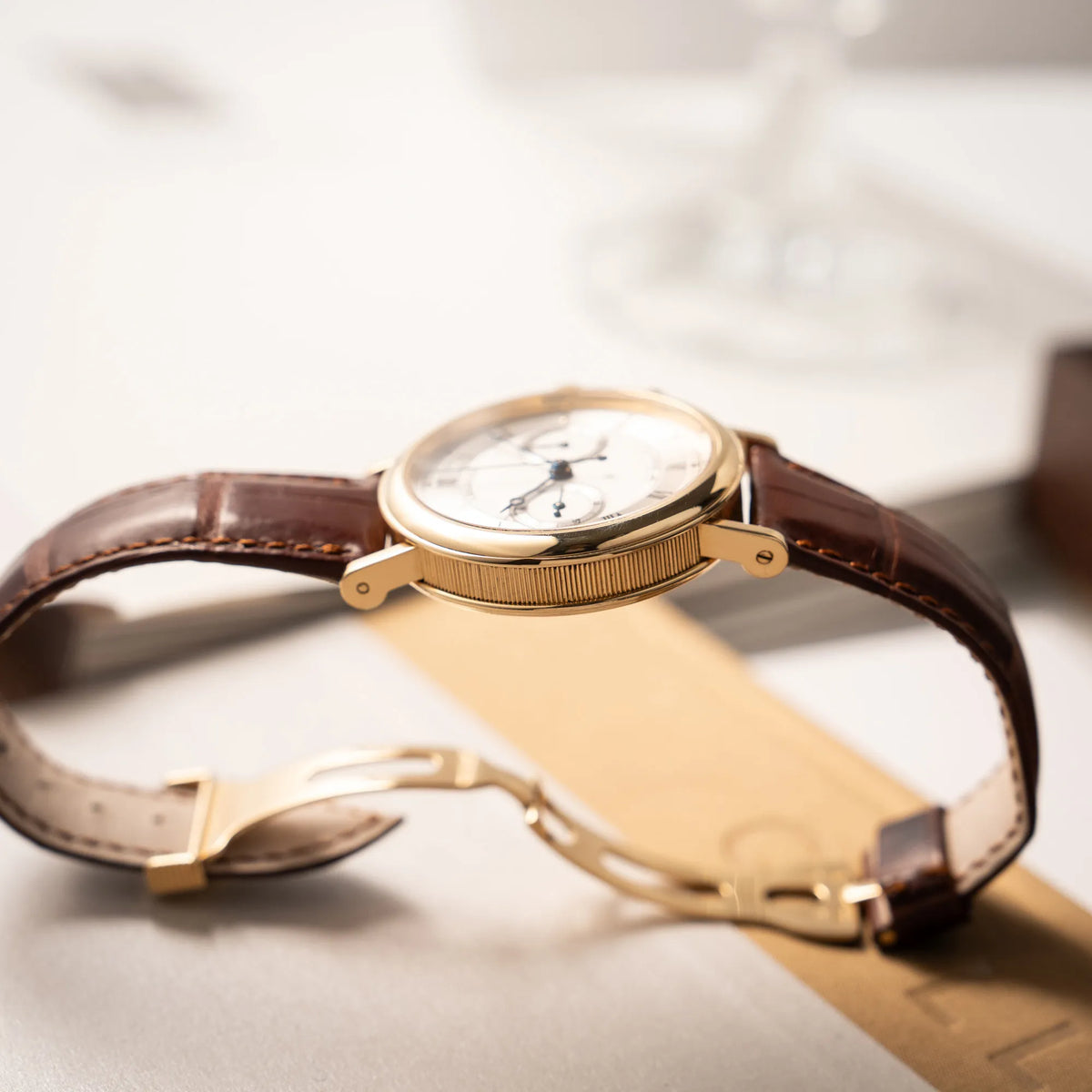 Produktfotografie ds Breguet Classique Chronograph der Referenz 5237 in Gelbgold mit silbernem guillochiertem Zifferblatt am braunem Lederband zeigt die kannelierte Gehäusflanke der Armbanduhr