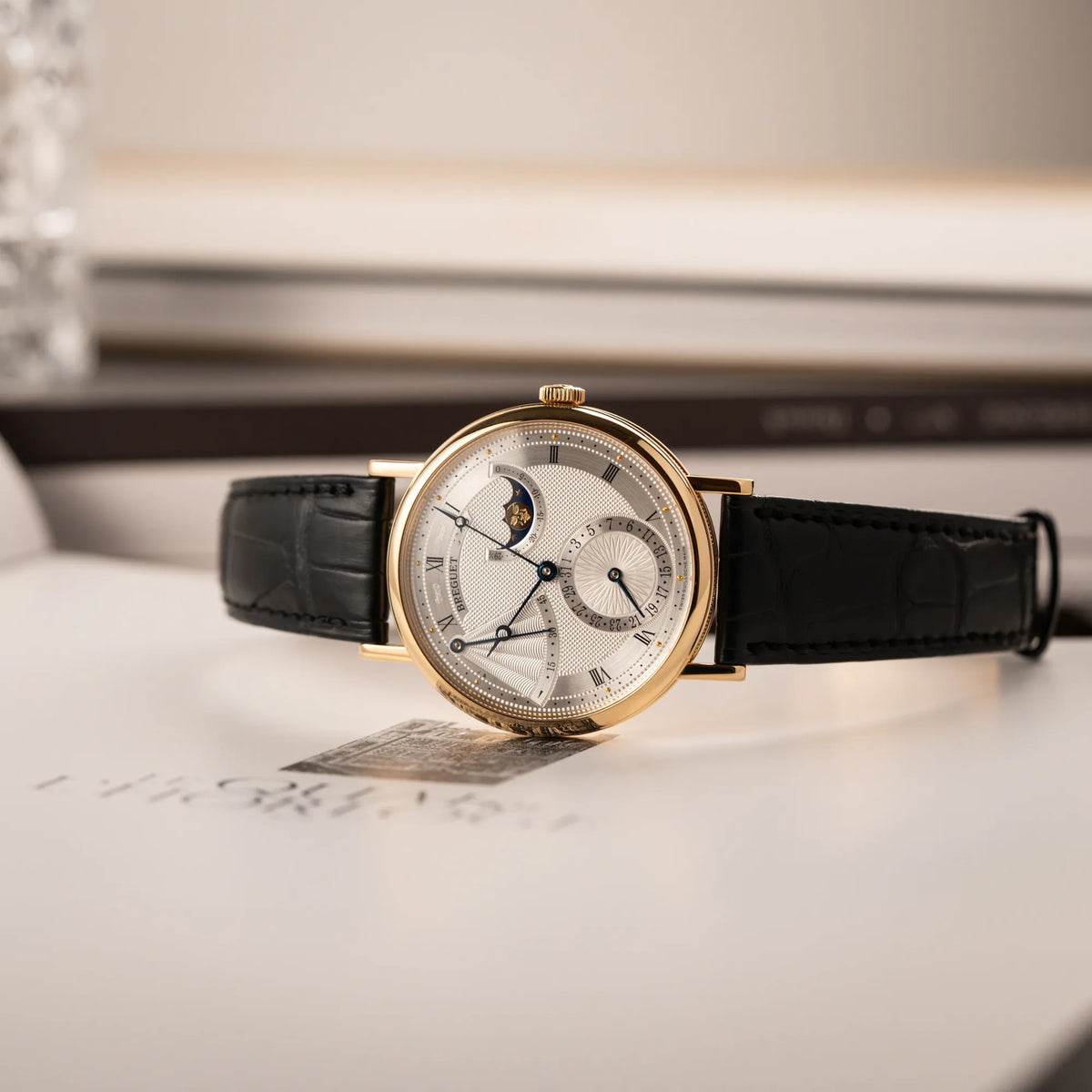 Produktfotografie der seitlich liegenden Breguet Classique Mondphase 7137 in Gelbgold mit silbernen, verschieden guillochiertem Zifferblatt