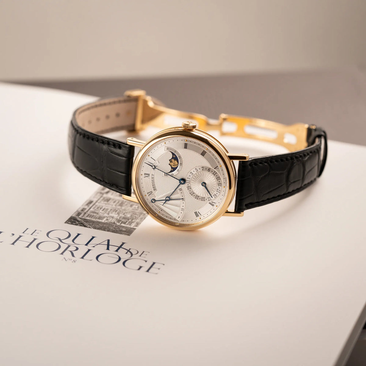 Breguet Classique Mondphase 7137 in Gelbgold mit silbernen, verschieden guillochiertem Zifferblatt liegt auf einem Breguet Buch