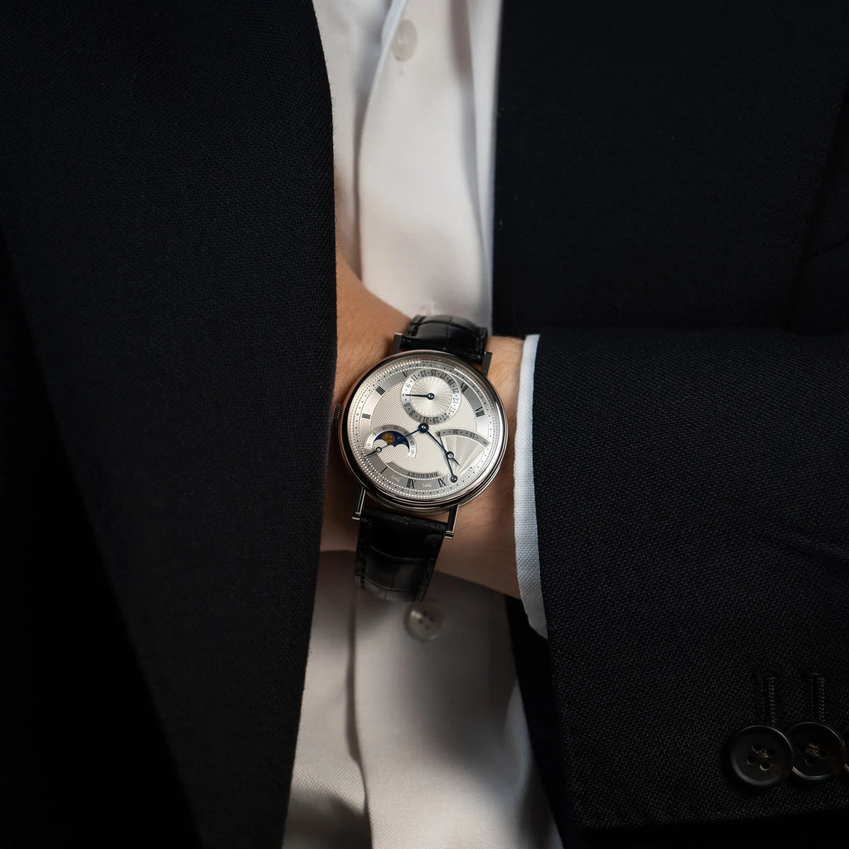 Mann im Anzug hat die Breguet Classique Moonphase der Referenz 7137 in Weissgold mit 3-fach guillochiertem Zifferblatt und Mondphase-Anzeige an seinem Handgelenk