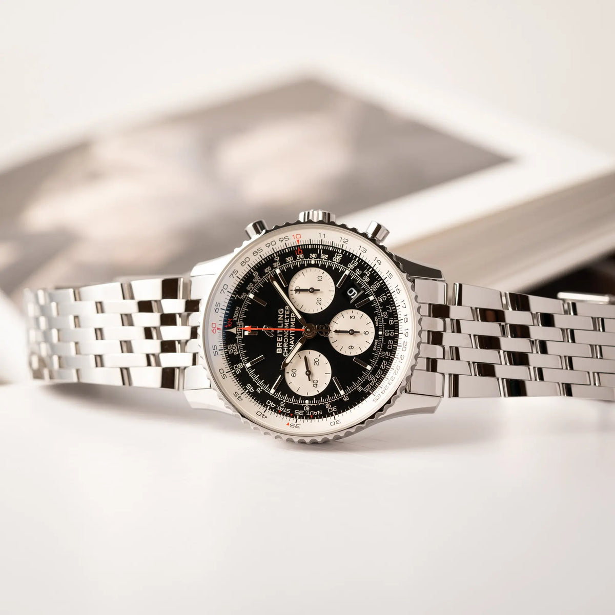 Breitling Navitimer B01 Chronograph der Referenz AB0121211B1A1 mit Reverse-Panda Zifferblatt in schwarz mit weißen Hilfszifferblätter liegt seitlich auf dem Uhrengehäuse