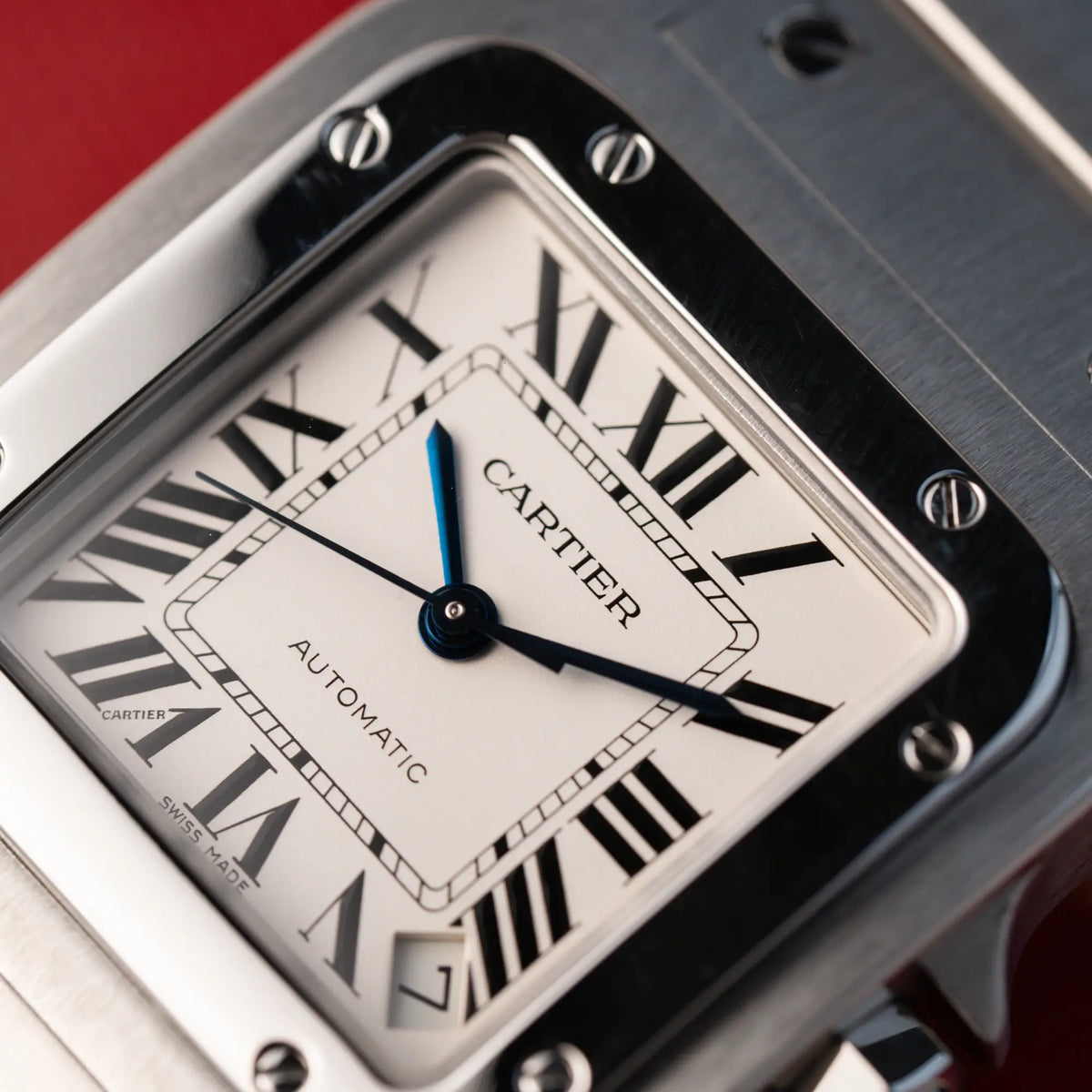 Detailaufnahme des weißen Zifferblatts mit römischen Indizes und blau-eloxierten Zeigern der Cartier Santos Galbée 2823 in Edelstahl
