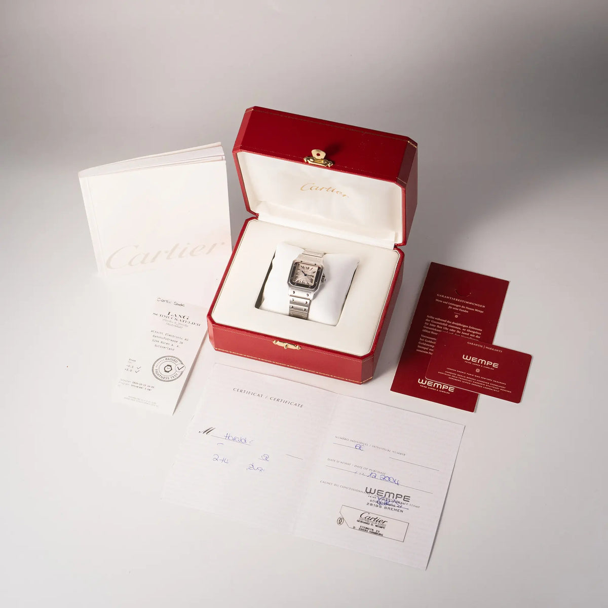 Lieferumfang zu der Cartier Santos Galbée 2913 in Edelstahl mit weiß-silbernem Zifferblatt am Stahlband mit der klassischen Cartier-Schrauben-Optik, betsehend aus Box, Booklet, originaler Garantiekarte und Wasserdichtheitstest