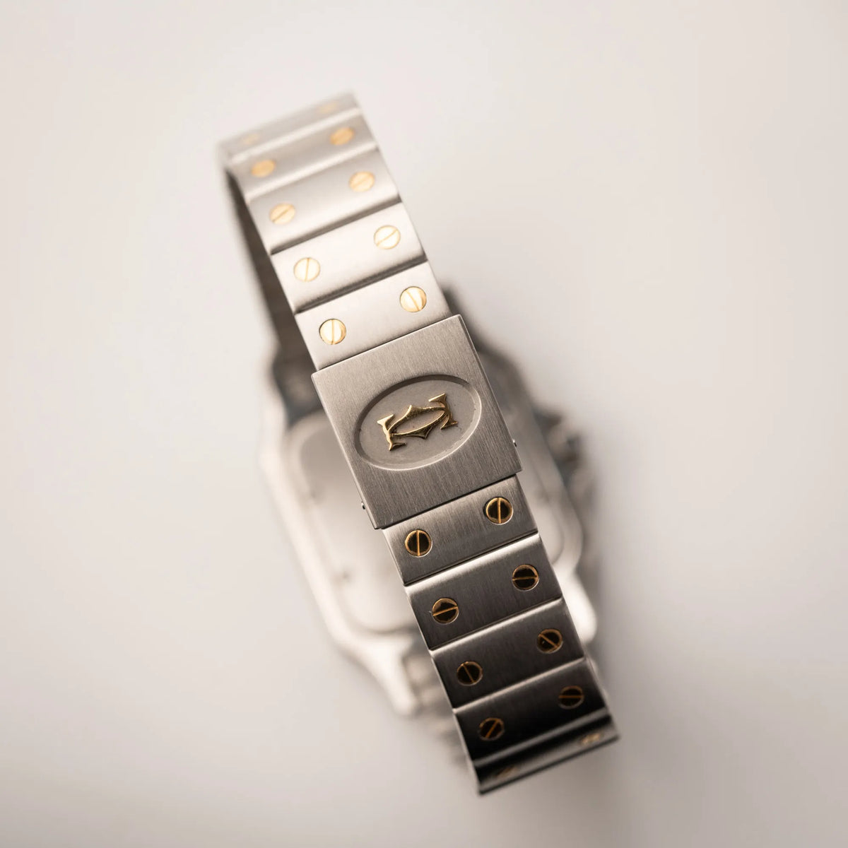 Detailaufnahme der geschlossenen Schliesse mit klassischem Cartier-Logo von der Cartier Santos Galbee BiColor der Referenz 187901 mit Stahl-Gold-Gehäuse am Stahlband mit dem Cartier-typischen Schrauben, die ebenfalls in Gelbgold gehalten sind, und einem cremfarbenen Zifferblatt mit klassischen römischen Indizes