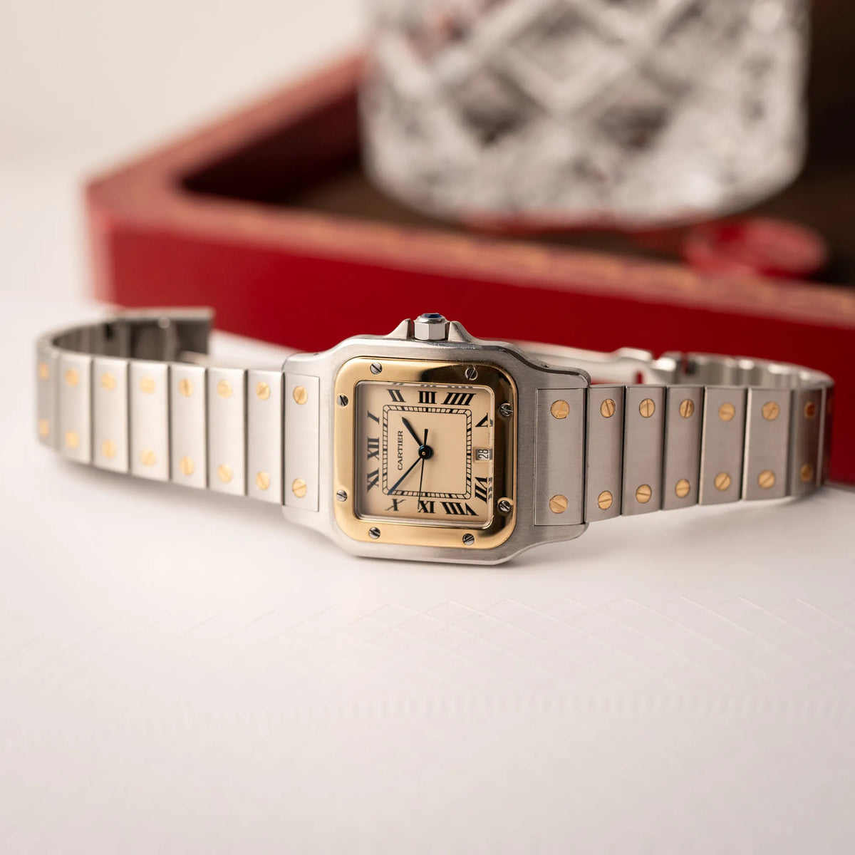 Produktfotografie zeigt die Cartier Santos Galbee BiColor der Referenz 187901 mit Stahl-Gold-Gehäuse am Stahlband mit dem Cartier-typischen Schrauben, die ebenfalls in Gelbgold gehalten sind, und einem cremfarbenen Zifferblatt mit klassischen römischen Indizes, während die Uhr seitlich auf dem Uhrengehäuse liegt