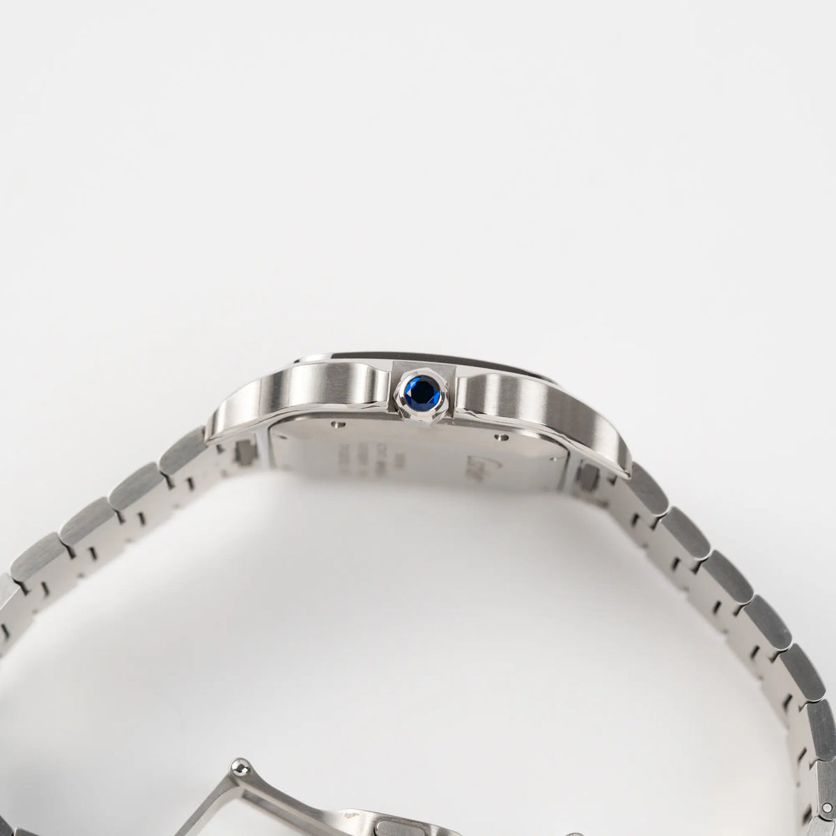 Seitliche satinierte Gehäuseflanke der Cartier Santos de Cartier als großes Modell der Referenz WSA0018 mit Blick auf die Aufzugskrone mit blauem Edelstein
