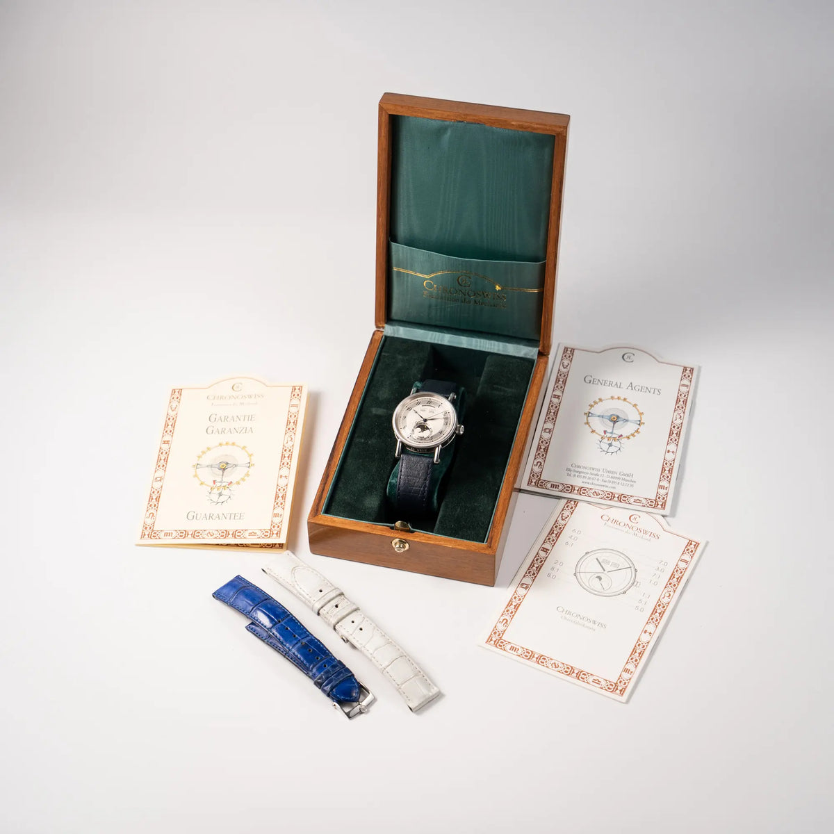 Lieferumfang zugehörig zu der Chronoswiss Klassic Luna Mondphase CH9323 mit silbernem, guillochiertem Zifferblatt mit Kalenderanzeige auf 12 Uhr und einer Mondphase-Anzeige bei 6 Uhr, bestehend aus Box, Papieren und zwei extra Lederbänder in Weiß und Blau