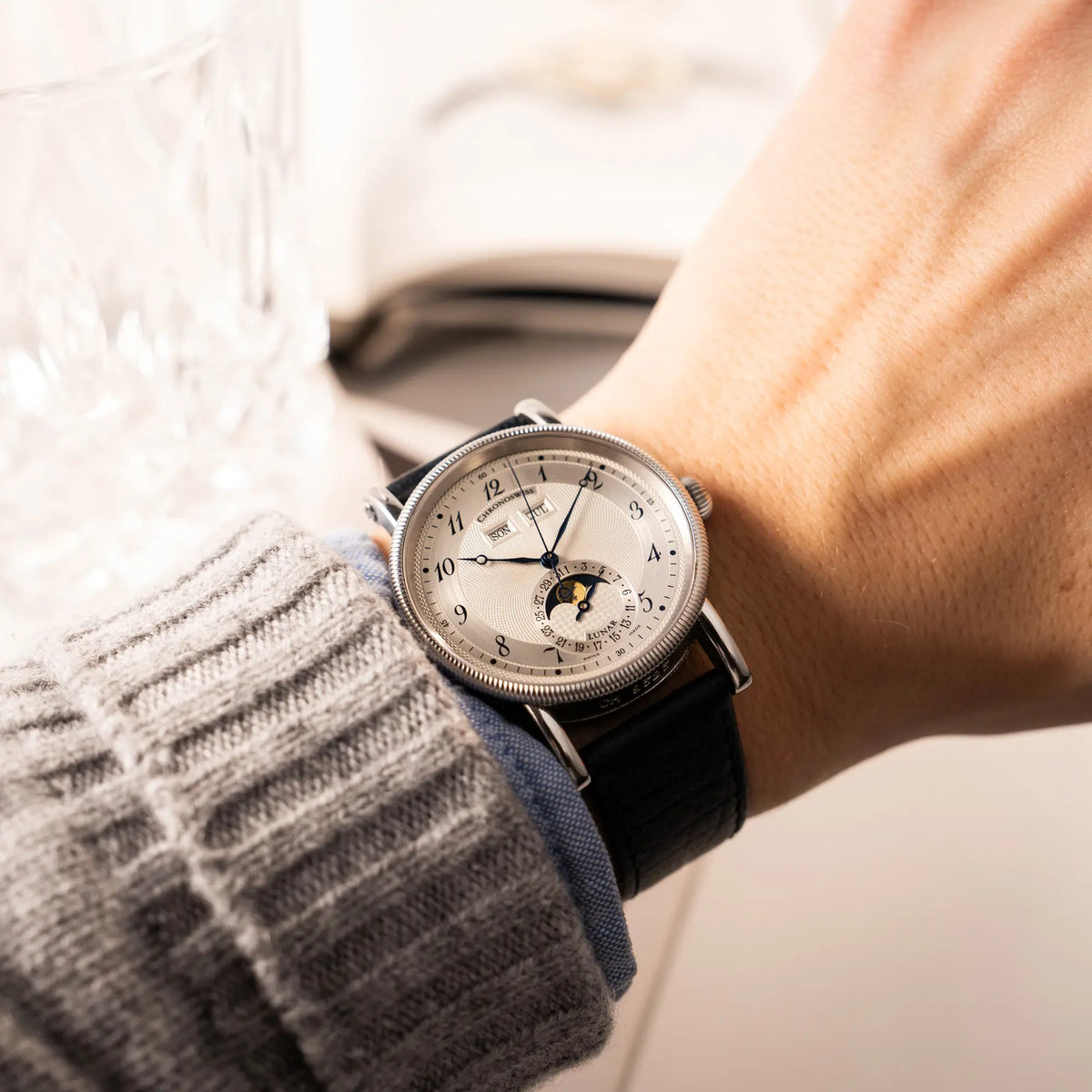 Wristshot mit der Chronoswiss Klassic Luna Mondphase CH9323 mit silbernem, guillochiertem Zifferblatt mit Kalenderanzeige auf 12 Uhr und einer Mondphase-Anzeige bei 6 Uhr