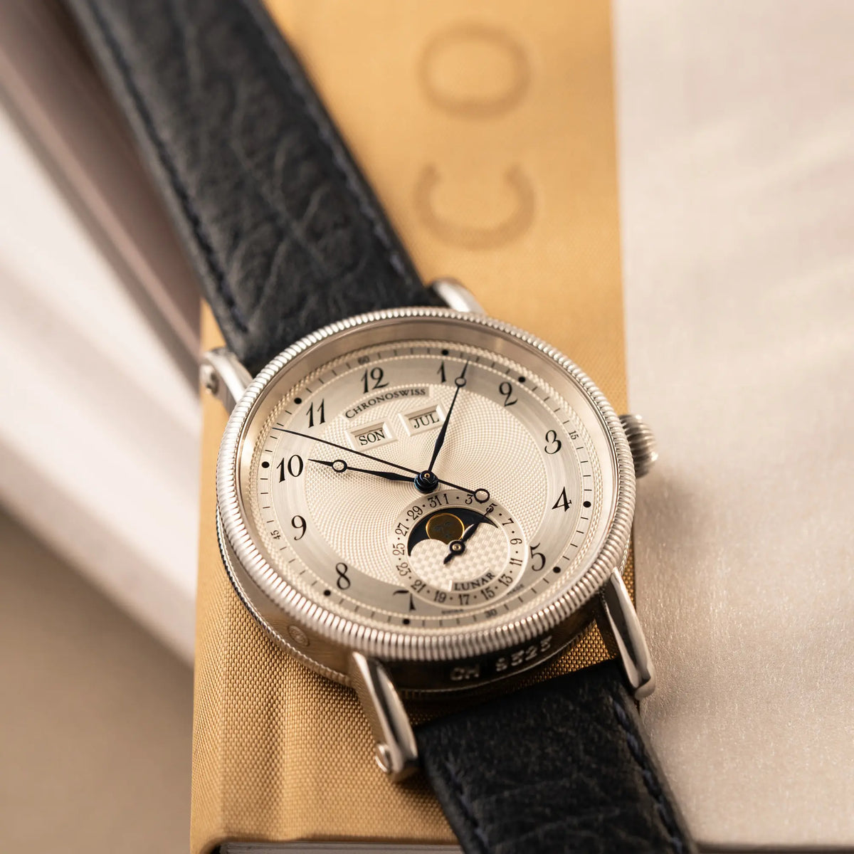Produktfotografie der Chronoswiss Klassic Luna Mondphase CH9323 mit silbernem, guillochiertem Zifferblatt mit Kalenderanzeige auf 12 Uhr und einer Mondphase-Anzeige bei 6 Uhr