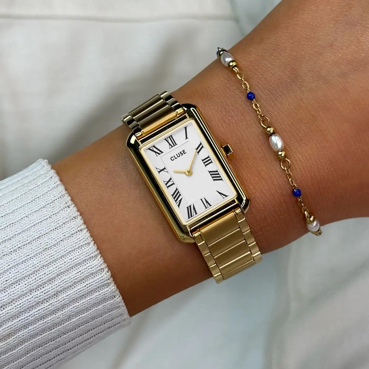 Wristshot mit der goldfarbenen Cluse Belisenna Damenuhr mit länglichem, rechteckigem Gehäuse und weißem Zifferblatt mit römischen Indizes