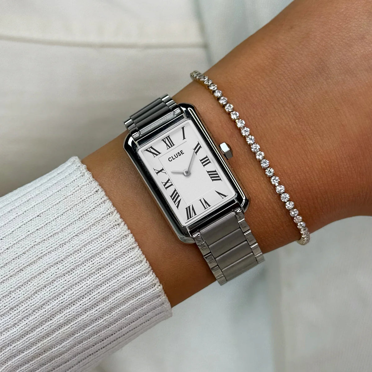 Wristshot mit der silberfarbenen Cluse Belisenna Damenuhr mit länglichem, rechteckigem Gehäuse und weißem Zifferblatt mit römischen Indizes