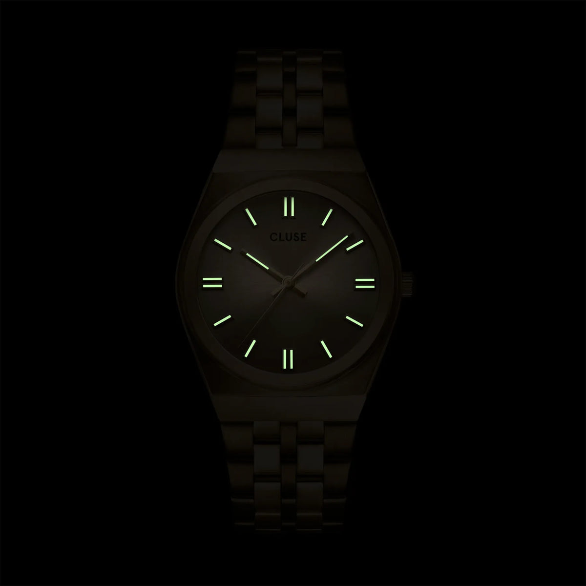 Blick auf das Zifferblatt mit leuchtenden Indizes und Zeigern der goldfarbenen Cluse Damenuhr Retro 70s der Referenz CW35104 mit integriertem Armband und goldfarbenem Zifferblatt