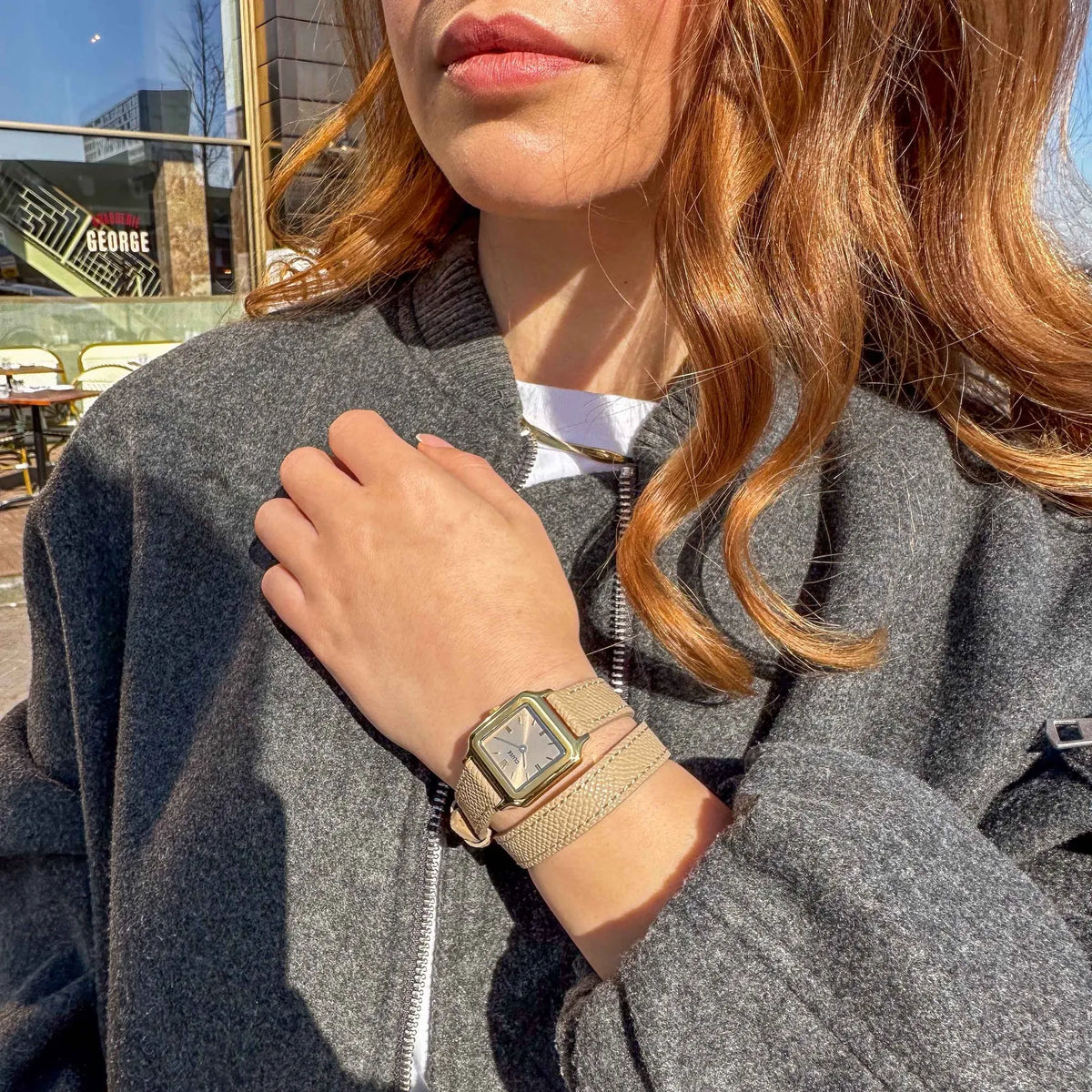 Lifestyleshot einer Frau mit der der goldfarbenen Cluse Gracieuse Petite Damenuhr mit rechteckigem Gehäuse und beigem/bronze-farbenem Zifferblatt an einem Doppel-Armband aus Leder im gleichen Farbton wie das Zifferblatt