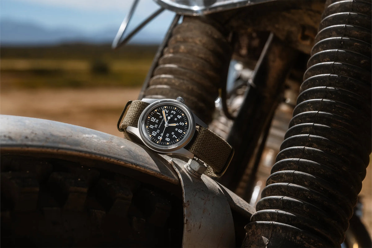 Lifestyle-Bild zeigt die Hamilton Khaki Field Watch Mechanical mit schwarzem Zifferblatt, während die Uhr auf dem Reifen eines Motorrads