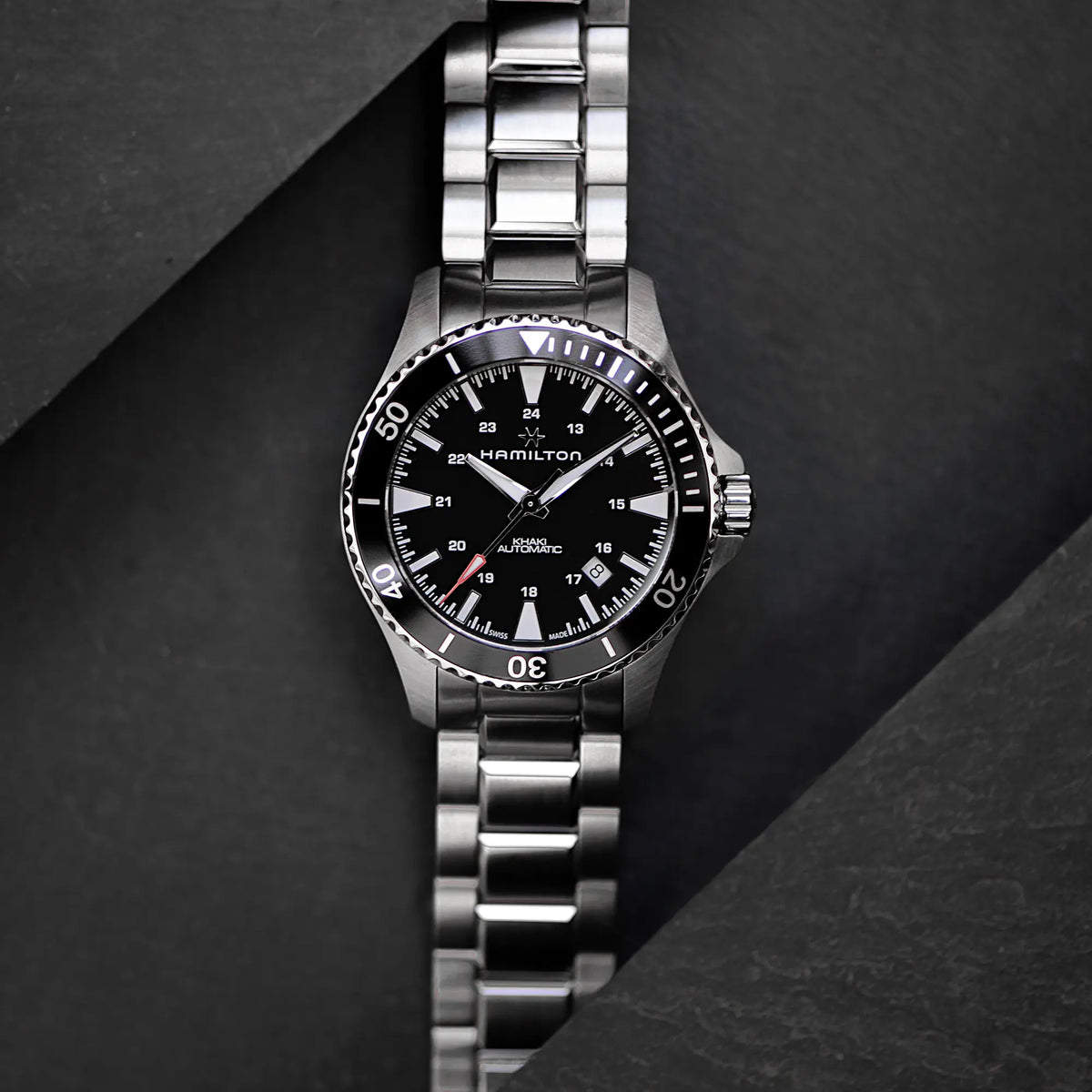 Künstlerische Produktdarstellung der Hamilton Taucheruhr Khaki Navy Scuba Auto H82335131 im 40mm-Edelstahlgehäuse mit schwarzem Zifferblatt und Lünette am Edelstahl-Armband