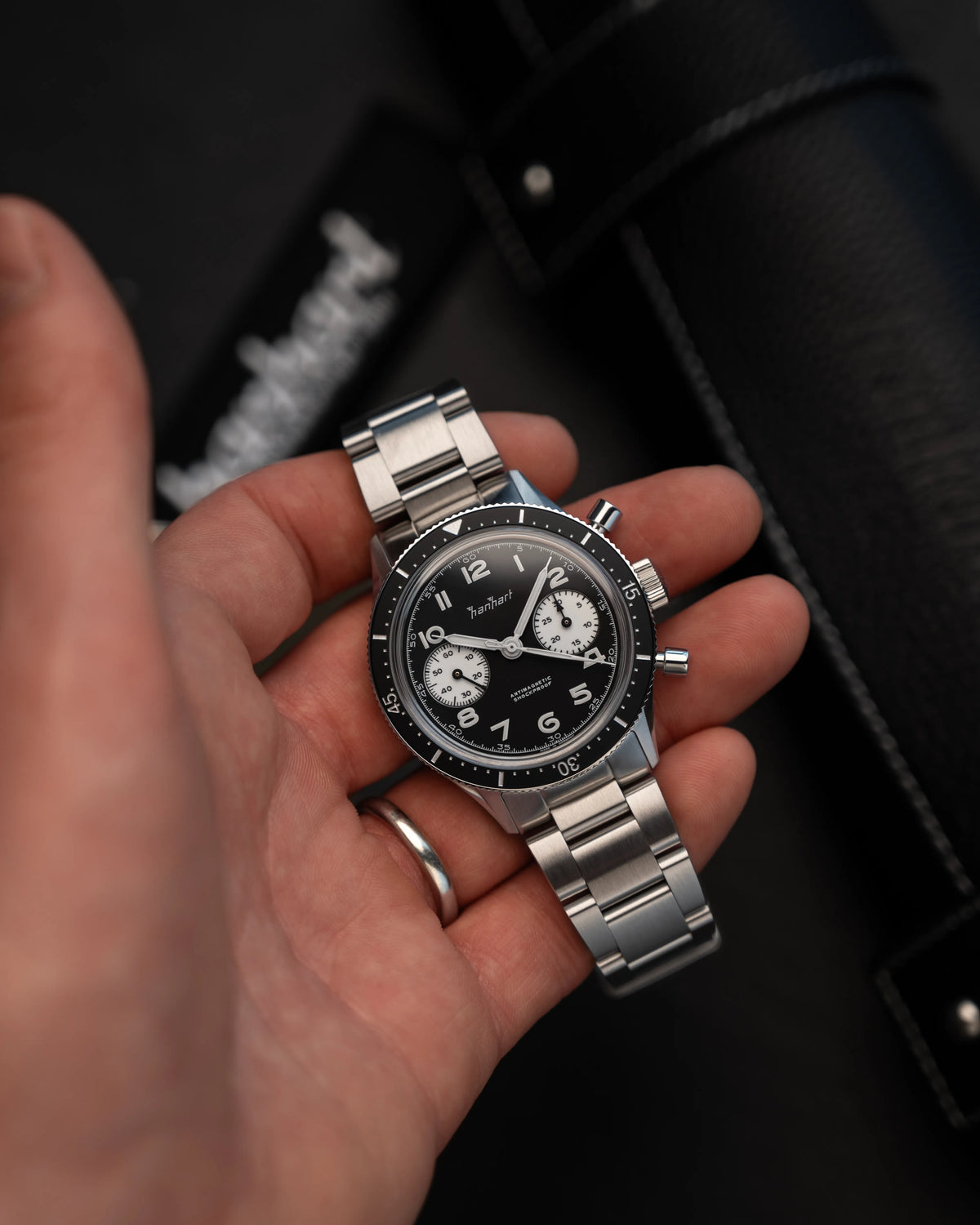 Mann präsentiert den Hanhart 415 ES Chronograph mit dem Reverse-Panda-Zifferblatt in Schwarz mit weißen Sub-Dials am Edelstahlarmband in die Kamera