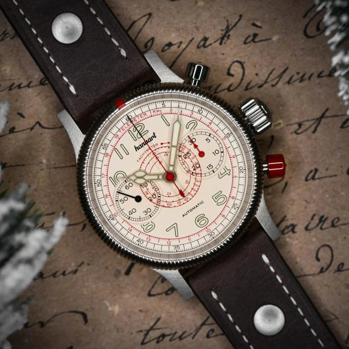 Produktfotografie des Hanhart Pioneer TachyTele Chronograph mit altweißem Zifferblatt und rot gehaltener Tachymeter-Skala und Telemeter-Skala am braunen Kalbslederband mit Niete