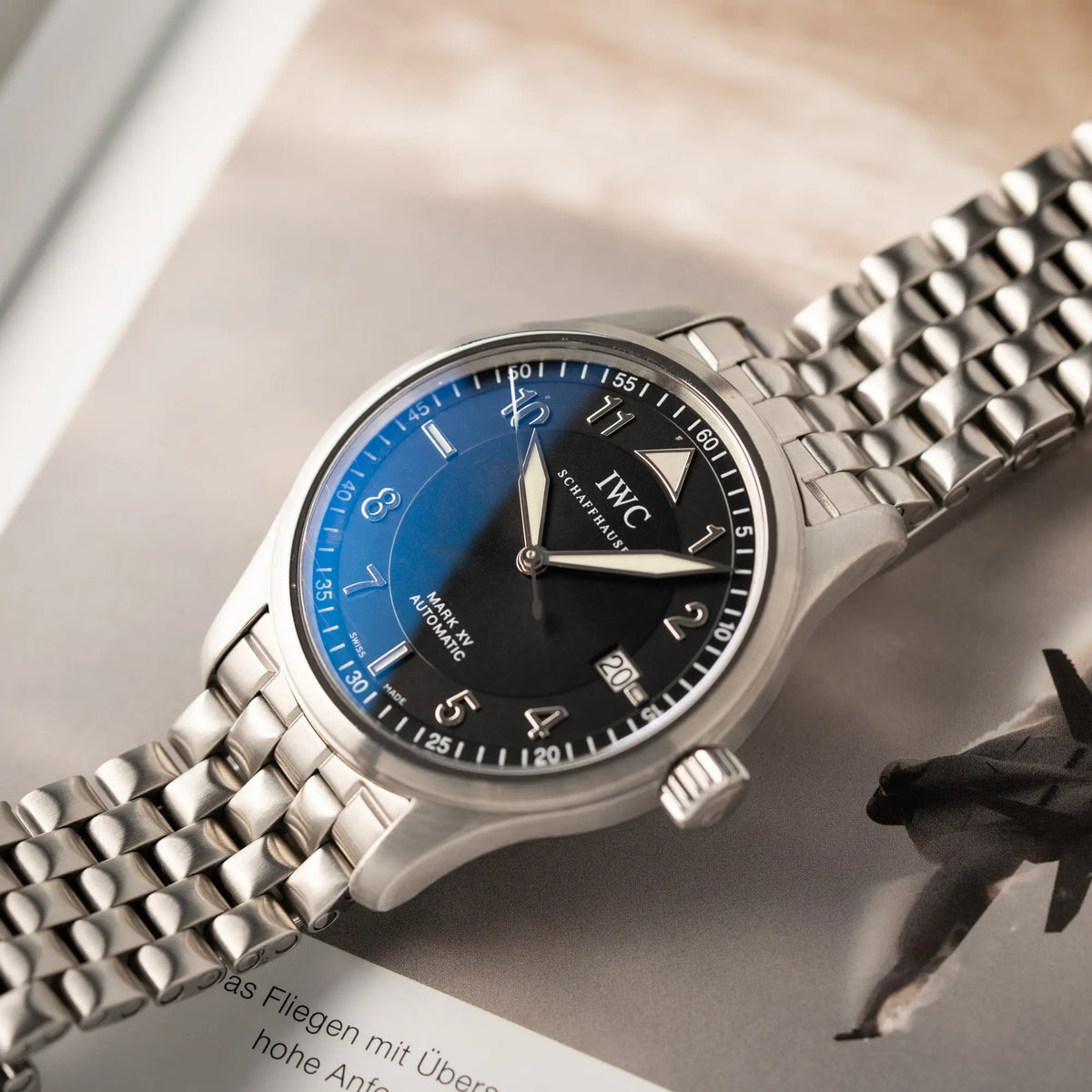 IWC Pilot Fliegeruhr Mark 15 der Referenz IW325312 aus 2005 mit dem schwarzen Zifferblatt an dem passenden, originalen 5-gliedrigen Stahlband liegt auf einem Buch über Fliegeruhr