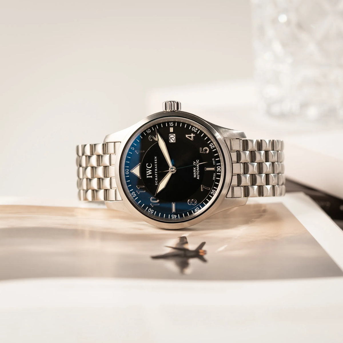 Produktfotografie der seitlich auf dem Uhrengehäuse liegenden IWC Pilot Fliegeruhr Mark 15 der Referenz IW325312 aus 2005 mit dem schwarzen Zifferblatt an dem passenden, originalen 5-gliedrigen Stahlband