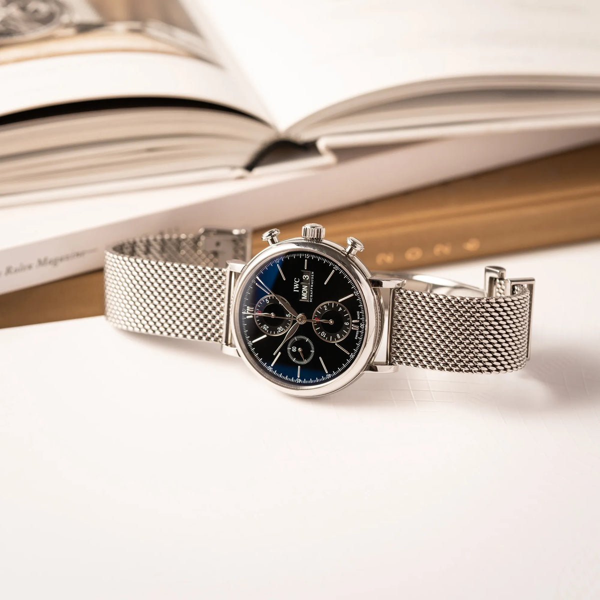 IWC Portofino Chronograph der Referenz IW391002 mit schwarzem Zifferblatt an einem Mesh-Armband liegt seitlich auf der Gehäuseflanke