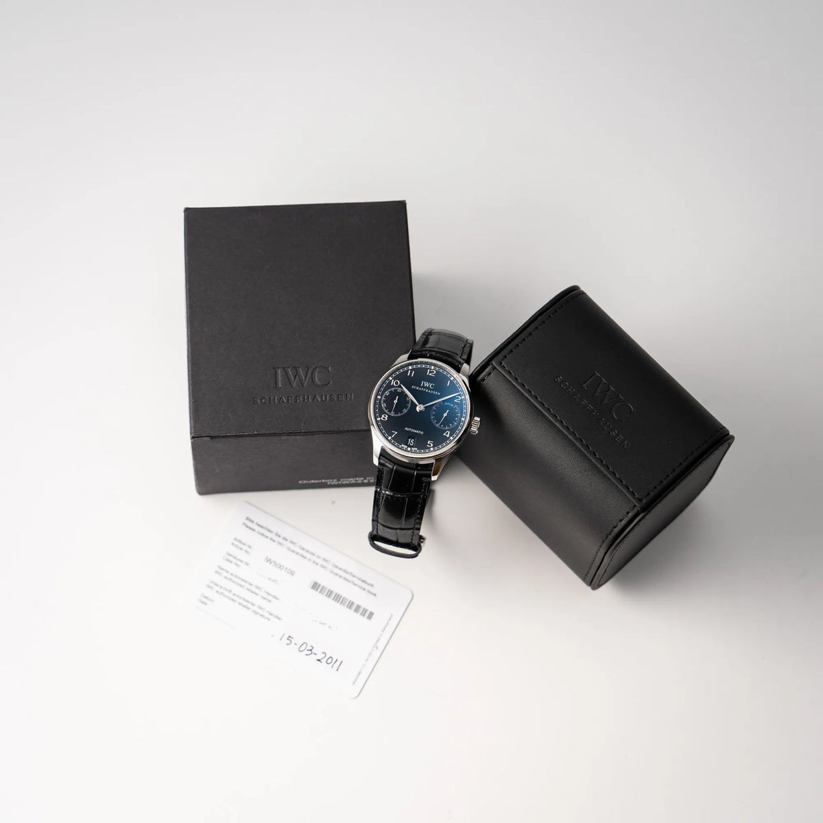 IWC Portugieser 7 Days IW500109 mit schwarzem Zifferblatt am schwarzen Lederband zusammen mit dem Lieferumfang, betsehend aus IWC Travel Box und Garantiekarte