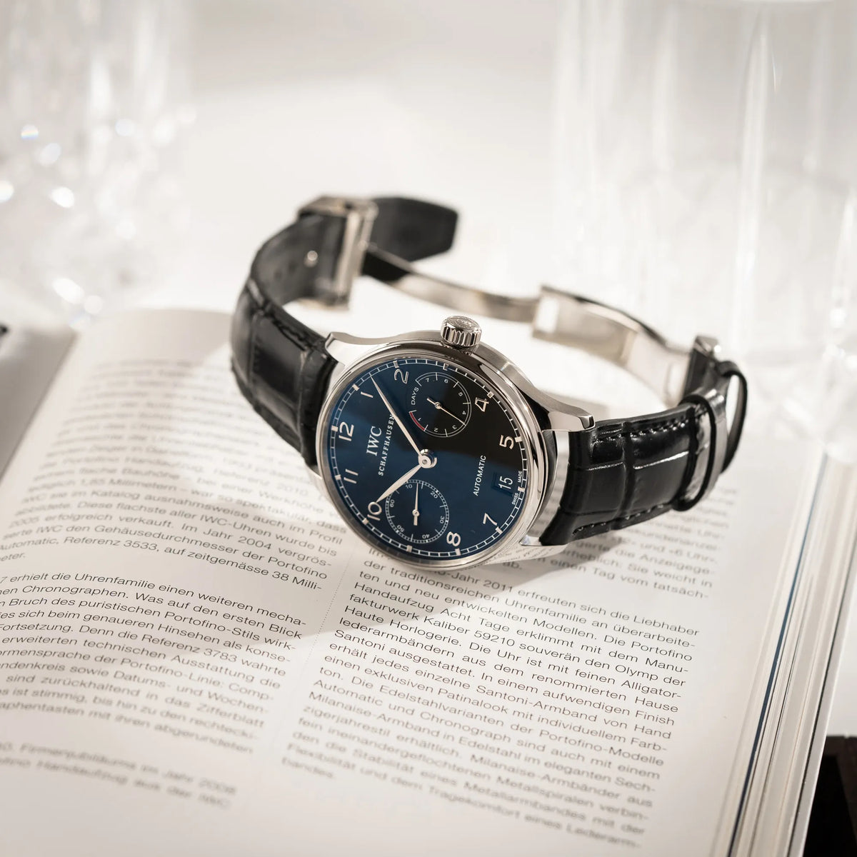 IWC Portugieser 7 Days IW500109 mit schwarzem Zifferblatt am schwarzen Lederband liegt auf einem Buch