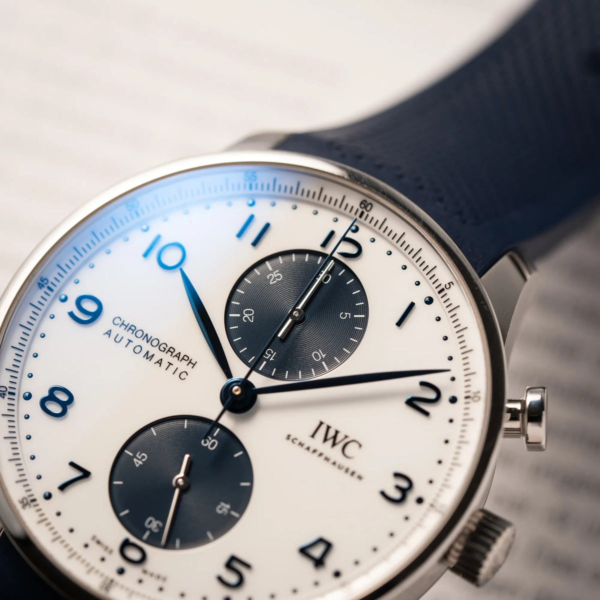 Detailaufnahme der IWC Portugieser Chronograph 41 der Referenz IW371620 mit weißem Zifferblatt und dunkelblauen Totalisatoren am passenden dunkelblauen Kautschukarmband zeigt den gebläuten Zeigersatz