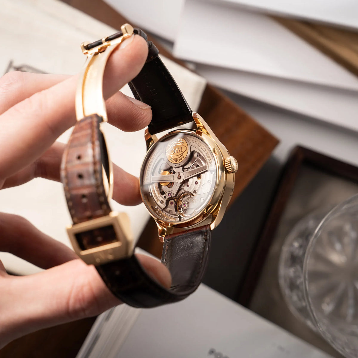 Mann hält den Portugieser Ewiger Kalender IW502213 von IWC in einem 42mm-Rosegold-Gehäuse am braunem IWC Lederband mit einem sanften weißem Zifferblatt in seiner Hand und präsentiert das Uhrwerk durch den gläsernen Gehäuseboden