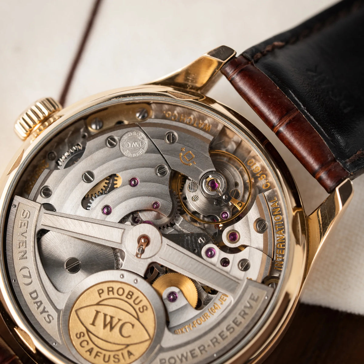 Produktfotografie zeigt das komplizierte Automatik-Uhrwerk des Portugieser Ewiger Kalender IW502213 von IWC in einem 42mm-Rosegold-Gehäuse am braunem IWC Lederband mit einem sanften weißem Zifferblatt durch den gläsernen Gehäuseboden