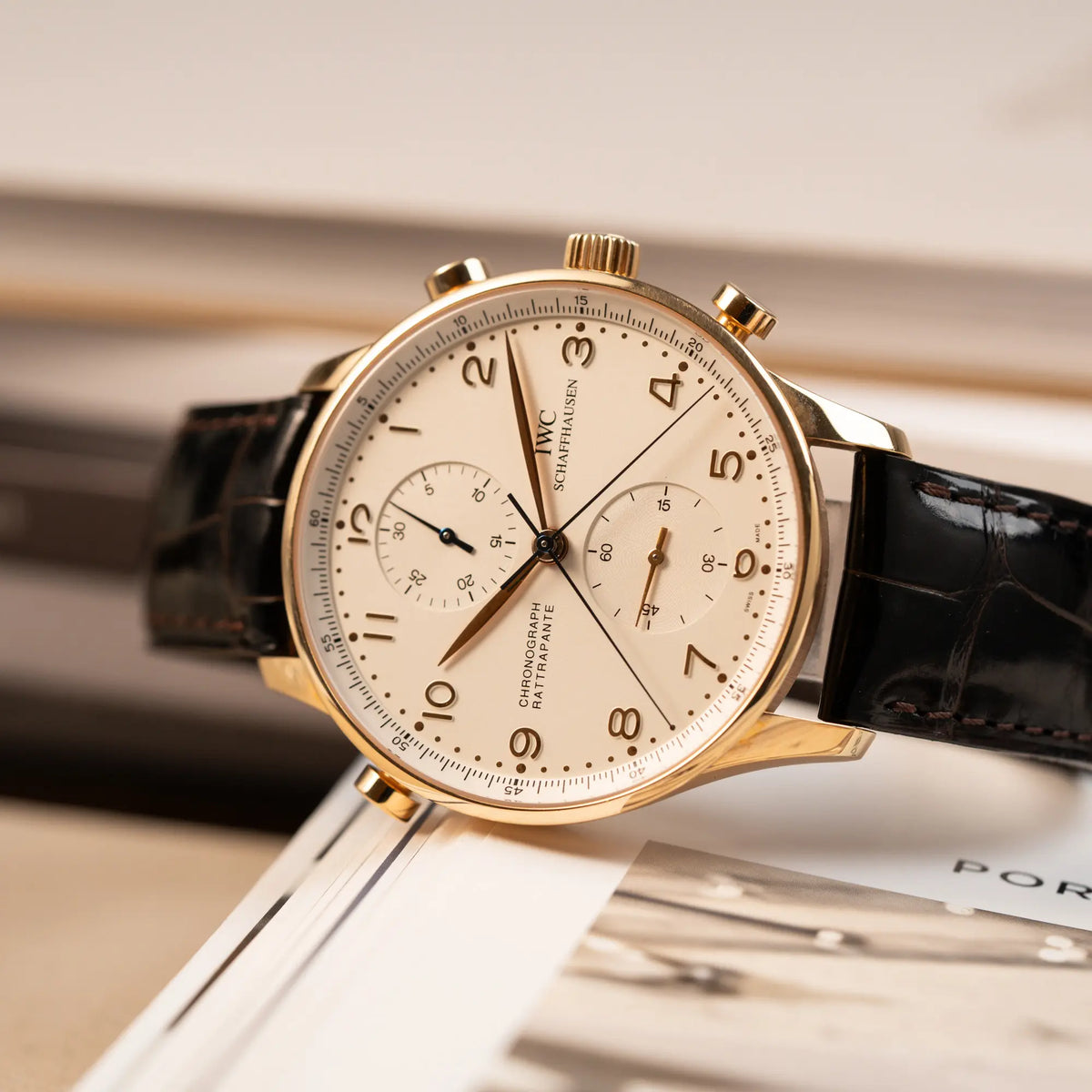 Produktfotografie der seitlich auf dem Gehäuse liegenden IWC Portugieser Rattrapante Doppel-Chronograph IW3712 aus 18k Roségold mit weißem Zifferblatt am braunen Lederband