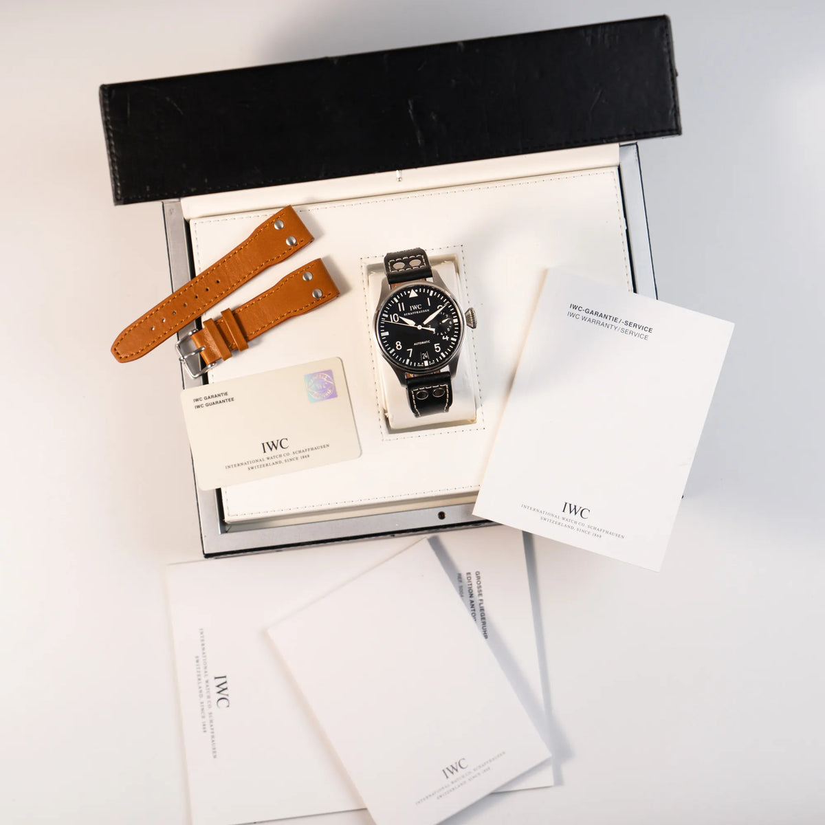 IWC Big Pilot 46 Armbanduhr der Referenz IW500401 mit schwarzem Zifferblatt und der Power-Reserve-Anzeige bei 3 Uhr zusammen mit dem Lieferumfang, betsehend aus zusätzlichem hellbraunem Lederband, Garantiekarte, Box und Booklets