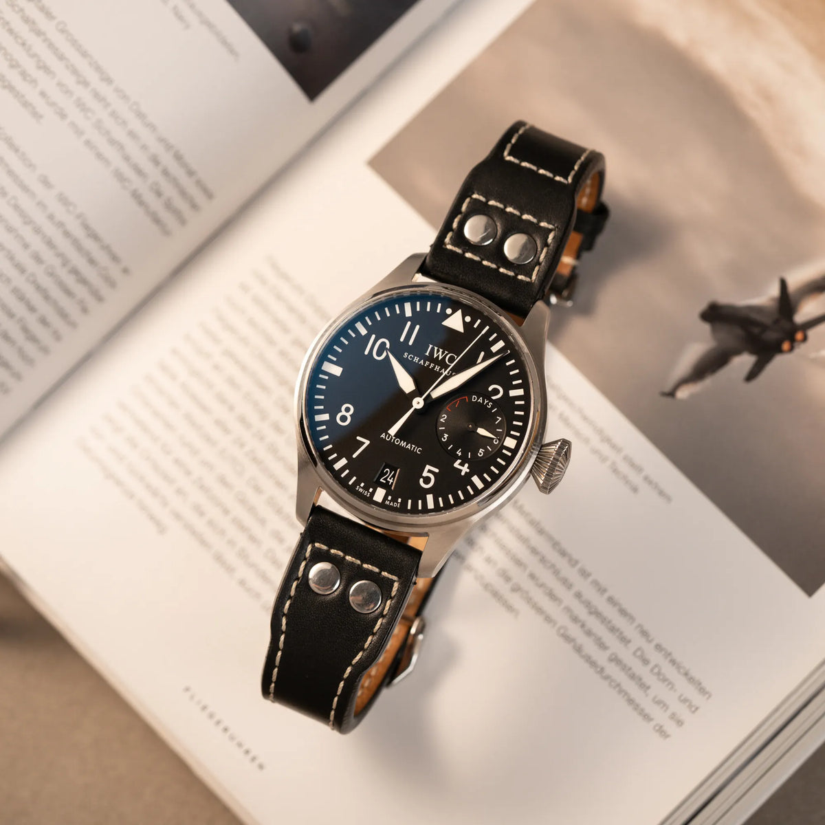 Produktfotografie der IWC Big Pilot 46 Armbanduhr der Referenz IW500401 mit schwarzem Zifferblatt und der Power-Reserve-Anzeige bei 3 Uhr über einem Fliegermagazin