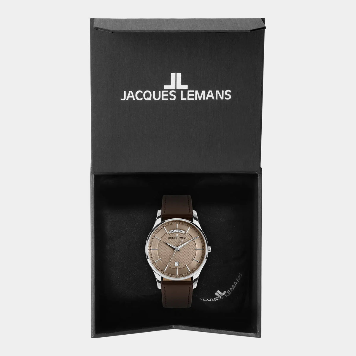 Jacques Lemans 1-2193K Derby Armbanduhr mit Tages und Datumsanzeige, welche farblich abgestimmt ist durch ein bronzefarbenes Zifferblatt und ein braunes Lederband liegt in der zugehörigen Uhrenbox