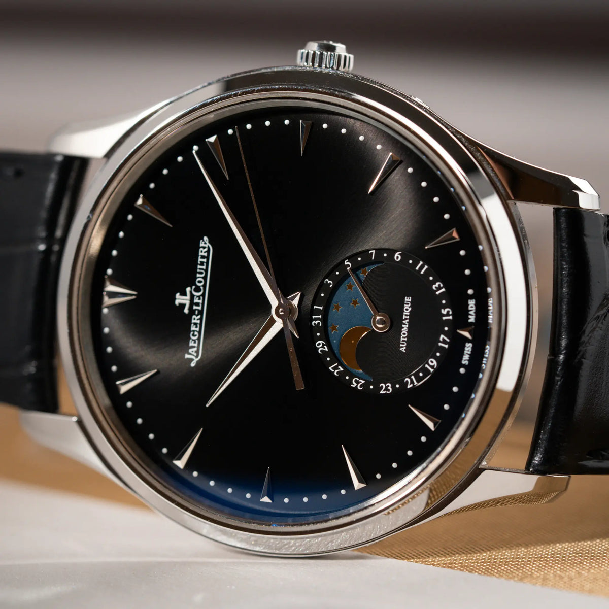 Detailaufnahme des seitlich auf dem Uhrengehäuse liegenden Jaeger-LeCoultre Master Control Q1368470 mit Datum und Mondphase in der schwarzen Zifferblattvariante