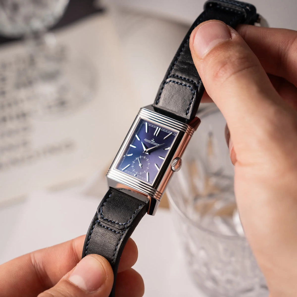 Mann präsentiert die Jaeger-LeCoultre Reverso Duoface Q3988482 mit blauem Zifferblatt und weißem Night-and-Day-Zifferblatt am schwarzen Lederband