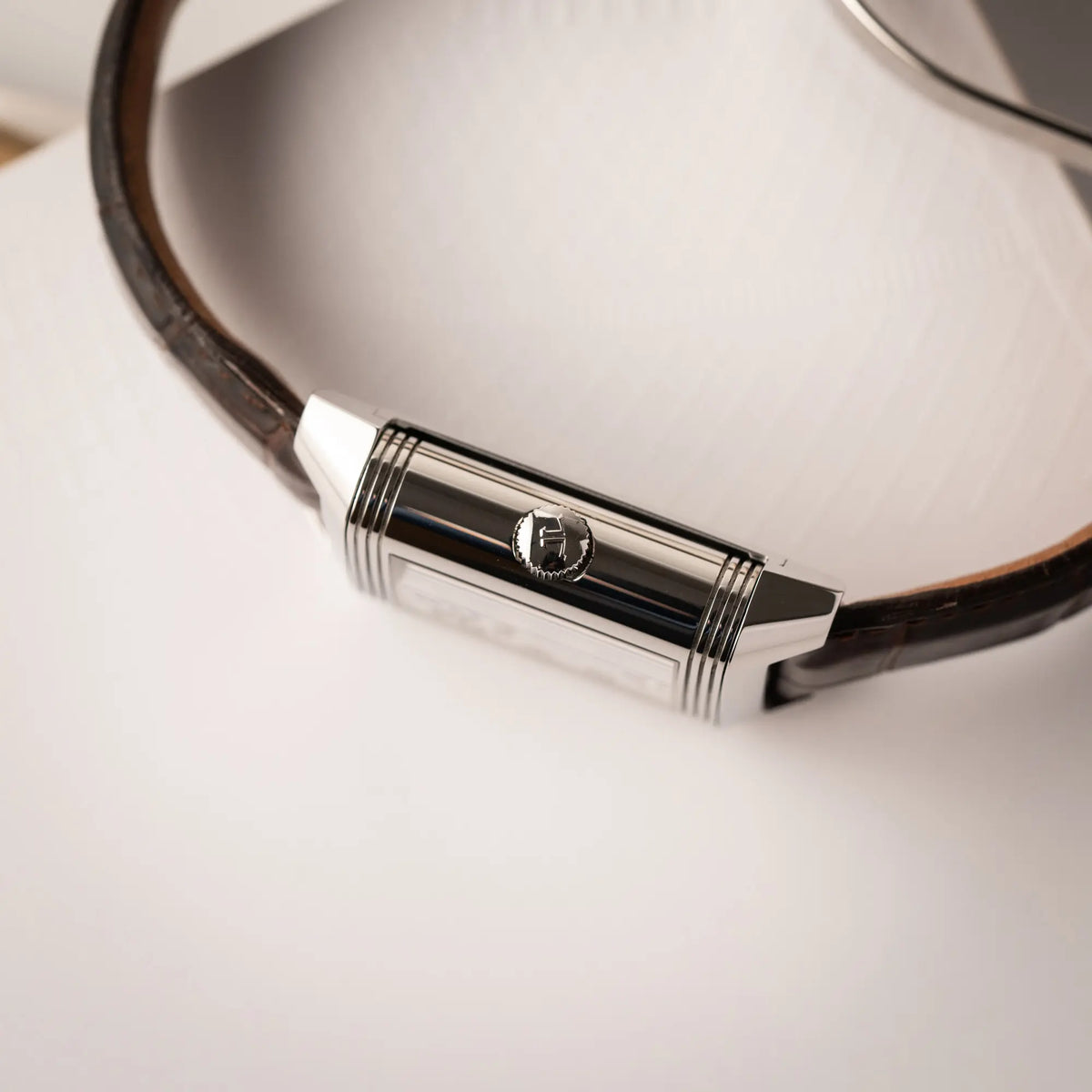 Produktfotografie der Jaeger-LeCoultre Reverso Grande Date der Referenz 240.8.15 mit silberfarbenem Zifferblatt und Großdatums-Anzeige, kleiner Sekunde und Gangreserve-Anzeige am braunen Lederband, zeigt die Aufzugskrone
