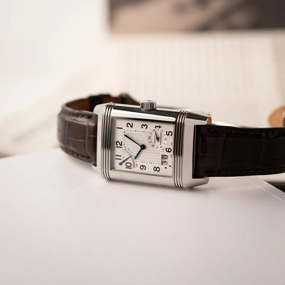 Jaeger-LeCoultre Reverso Grande Date der Referenz 240.8.15 mit silberfarbenem Zifferblatt und Großdatums-Anzeige, kleiner Sekunde und Gangreserve-Anzeige am braunen Lederband liegt seitlich auf der Gehäusflanke