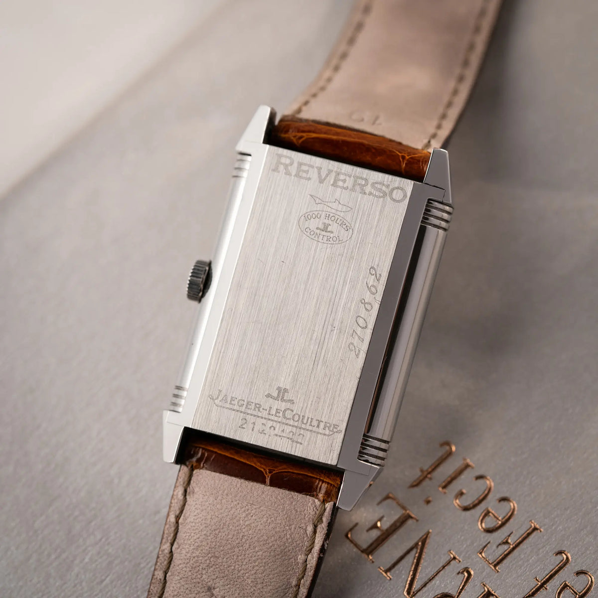 Produktfotografie der Jaeger-LeCoultre Reverso Grande Taille der Referenz 270.8.62 mit einem teil-guillochiertem, silberfarbenem Zifferblatt an einem braunem Lederband an seinem Handgelenk zeigt den Gehäuseboden mit allen typischen Gravuren